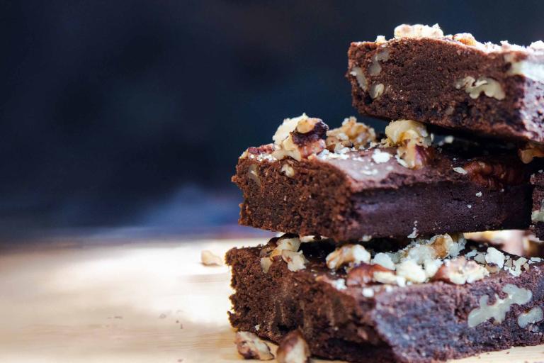 A stack of chocolate and pecan brownies, sprinkled with pecan crumbs and crushed walnut, fresh out of the oven